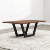 The Addison Coffee Table features a modern rectangular design with a dark brown finish and black V-shaped metal legs. Placed on a light-colored, textured rug in a minimalist room with light gray walls and wood flooring, the scene is bathed in natural light.