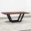 The Addison Coffee Table showcases a distinctive thick dark brown rectangular wooden surface, which rests gracefully on a patterned area rug. Its unique black metal base creates an inverted trapezoid shape, imparting a modern and geometric touch to the space against a plain white wall.