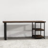 The Loredo Desk is a simple, modern writing desk with a dark Loredo wooden surface and three wooden shelves on the right side, supported by a black metal frame. It stands on a light gray floor and is set against a plain white wall, partially covering a textured light gray rug.