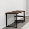 The Loredo Desk is a minimalist wooden console table featuring a dark brown top and two matching lower shelves, all supported by a sleek black metal frame. Positioned against a white wall, this piece of office furniture beautifully contrasts with the gray wooden floor and is partly overlaid by a rug below.