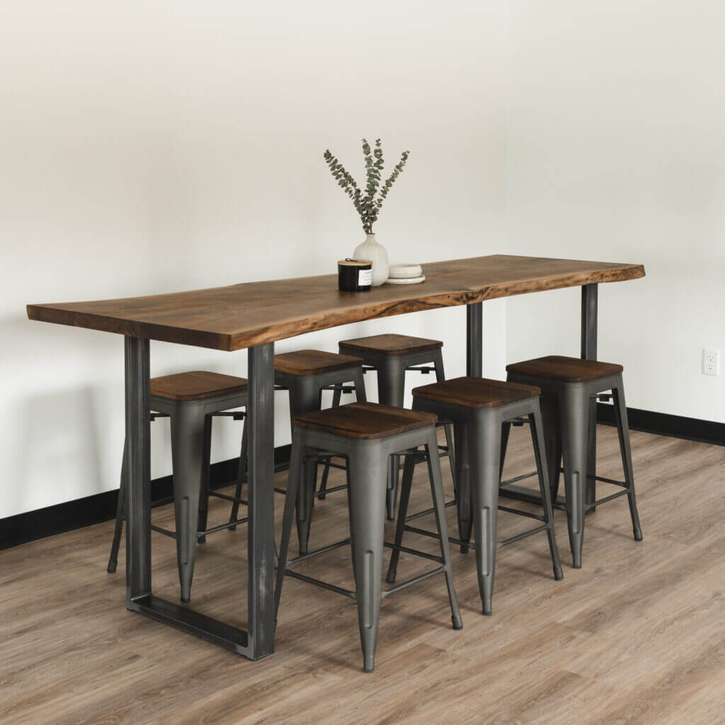 A modern dining area featuring the Black Walnut Live Edge Table with sleek U-shaped legs. Five metal stools with wooden seats are neatly arranged around the table. On the tabletop, two vases with dried foliage and a small black candleholder add charm.