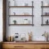 A kitchen featuring a white subway tile backsplash and wooden countertops, complete with an Industrial Hanging Pipe Shelf. The shelves are adorned with jars, mugs, a teapot, and a small potted plant, while wooden utensils sit neatly in a holder on the countertop.