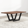The Addison Coffee Table, featuring a thick dark brown rectangular wooden top and V-shaped black metal legs, is placed on a light gray and white patterned rug over a light wood floor. A plain white wall serves as the background.