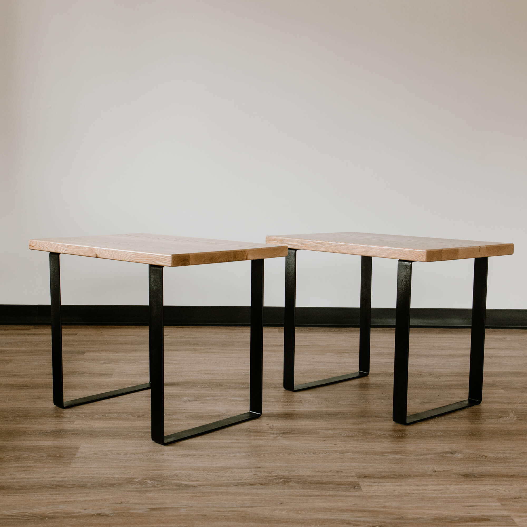Two minimalist rectangular wooden stools with smooth, light-colored seats and black metal legs complement The White Oak U-shaped End Table. Placed on a wooden floor against a plain, light background, the scene exudes simplicity and elegance.