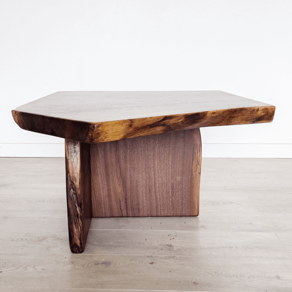 A wooden coffee table with a thick, irregularly shaped top and sturdy legs, showcasing a natural wood grain and texture. This piece of live edge furniture stands on a light wooden floor with a white wall background, embodying the latest in furniture trends.