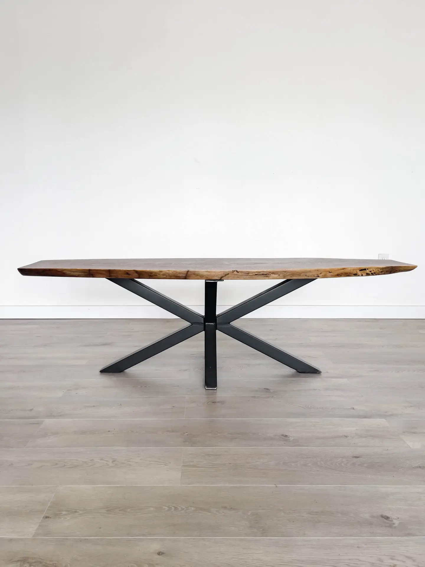 Introducing the Ready To Ship - Black Walnut Live Edge Coffee Table: a minimalist design crafted from rich black walnut wood and featuring black crisscross metal legs. This elegant piece is ready to ship and rests beautifully on a light gray hardwood floor against a plain white wall.