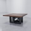The Westbrook Coffee Table, featuring a square wooden design with a dark brown polished surface and a modern, geometric black metal base, is positioned on a smooth, light gray floor in a minimalist room with white walls.